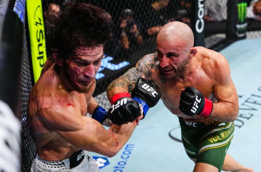 Two UFC fighters exchange punches in the cage, one getting cut on his face as blood drips from his nose.