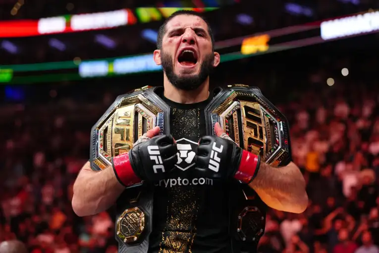 UFC champion wearing two championship belts, fists raised and shouting triumph in the arena.