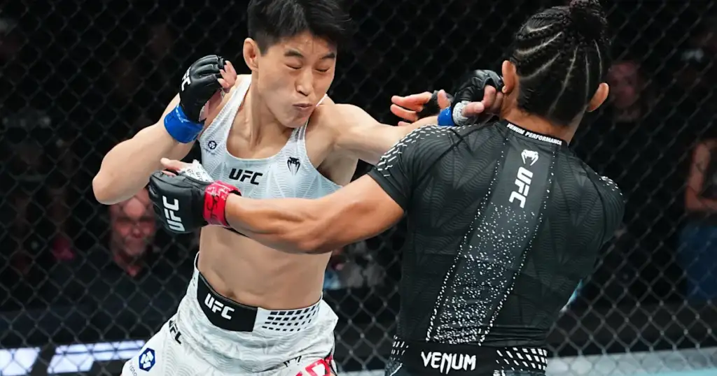 Two UFC fighters collide in a close-up exchange inside a cage, one delivering a punch while the other blocks with an extended arm guard.