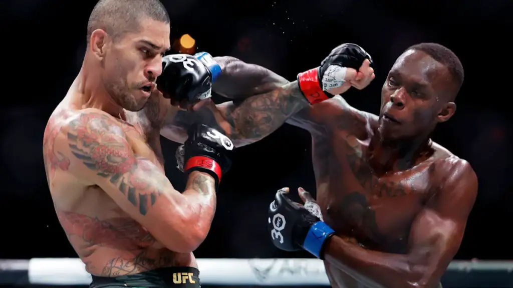 Two mixed martial artists fight in a UFC match; the left fighter lands a punch to his opponent's head as they exchange blows in the octagon with gloves and tattoos visible on their bodies.