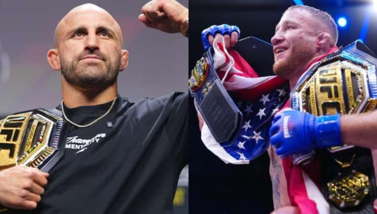 Two UFC champions pose with their belts, fist-bumping as a celebration; one wears a black shirt, the other holds an American flag and wears blue gloves on stage.