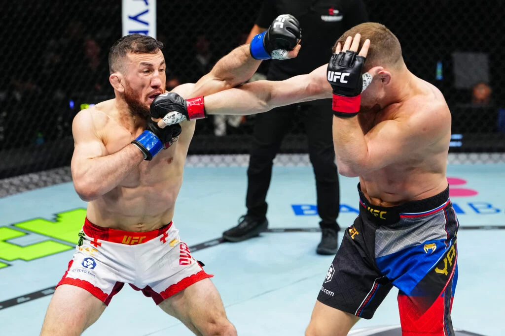 Two UFC fighters trade punches inside the octagon; the left fighter lands a blow to the right fighter as the referee watches.