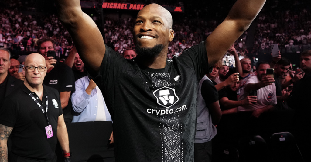 Athlete with arms raised in victory, wearing a black crypto.com shirt, crowd cheering behind him in a stadium.