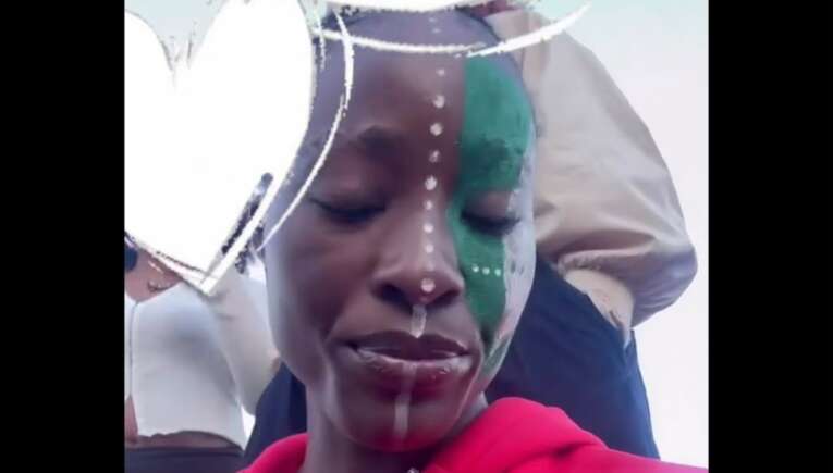 Close-up of a woman in a red hoodie, half her face painted green with white dot lines and a white overlay across the camera frame.
