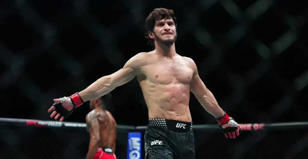 gettyimages-2267336138 - AfroCombat UFC fighter stands with arms outstretched in the octagon, celebrating victory after a match, another fighter in the background.