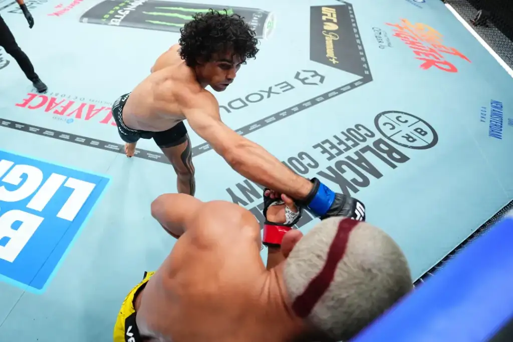 Two mixed martial artists in an octagon exchange a punch as one reaches toward the other’s glove during a bout.