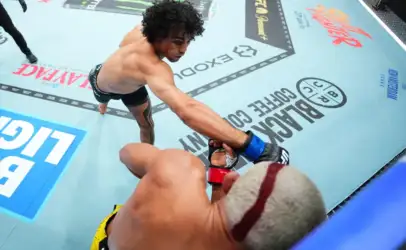 Two mixed martial artists in an octagon exchange a punch as one reaches toward the other’s glove during a bout.