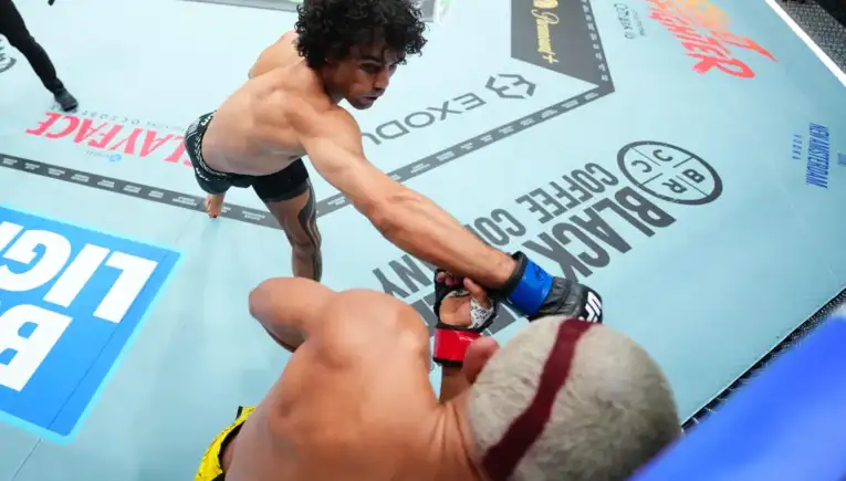 Two mixed martial artists in an octagon exchange a punch as one reaches toward the other’s glove during a bout.